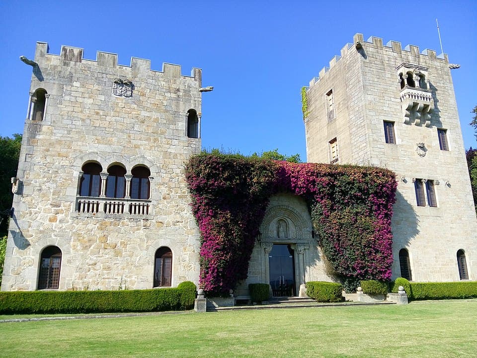 Stone castle with crenellated towers and ivy-covered archway entrance on a green lawn against a blue sky, photo-like scene.